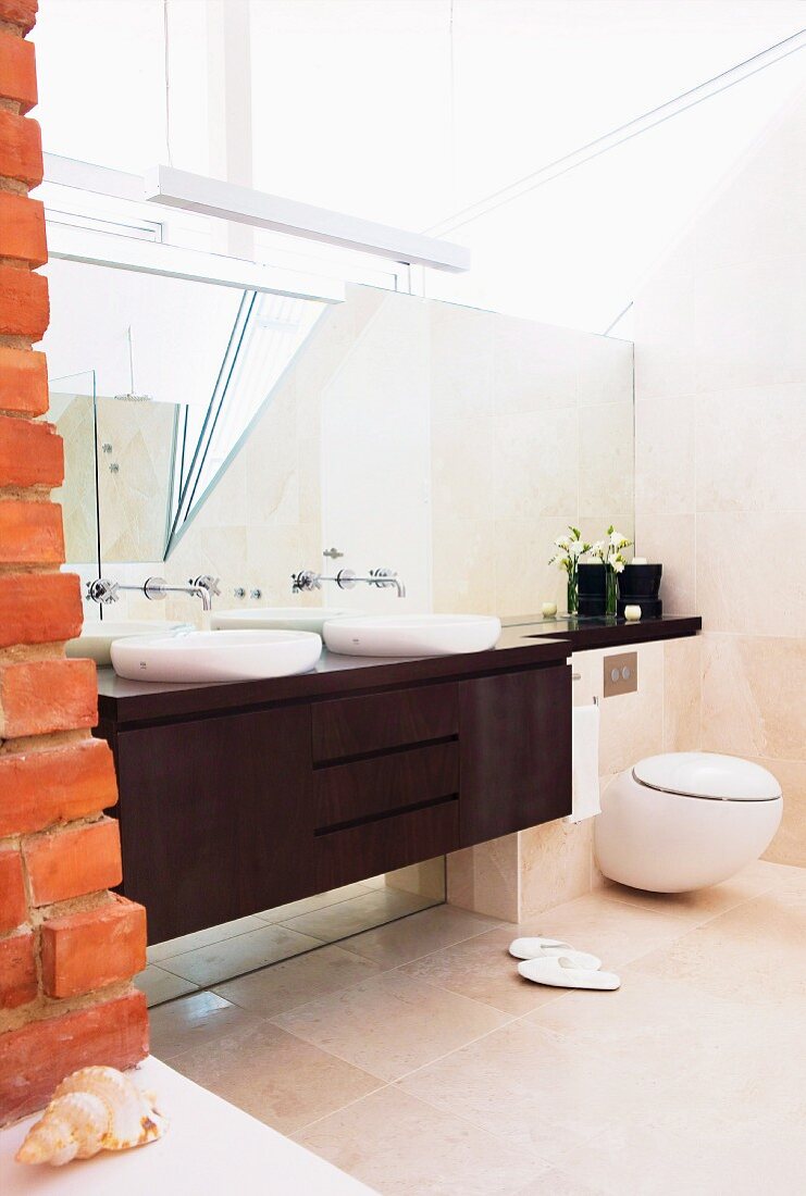 Brown washstand and base cabinet with two white, counter-top basins next to brick wall in designer bathroom