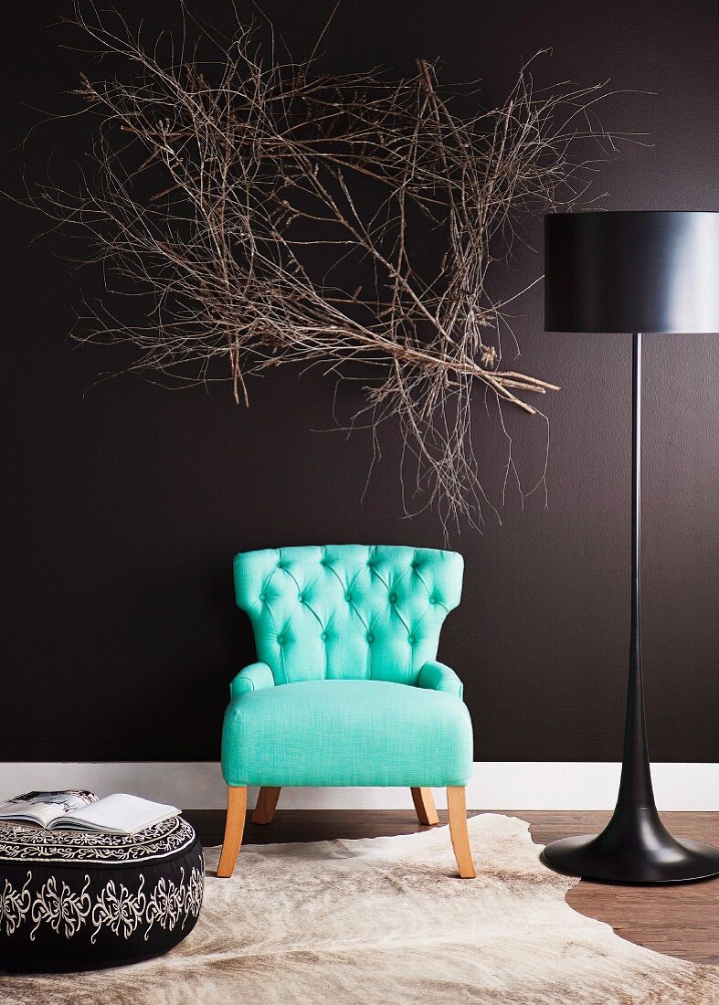 50's style turquoise armchair between modern floor lamps and upholstered ottoman in front of a black wall