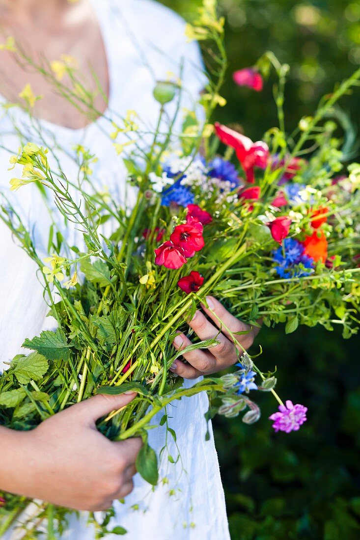 A woman holding a bunch of wild flowers in her arms