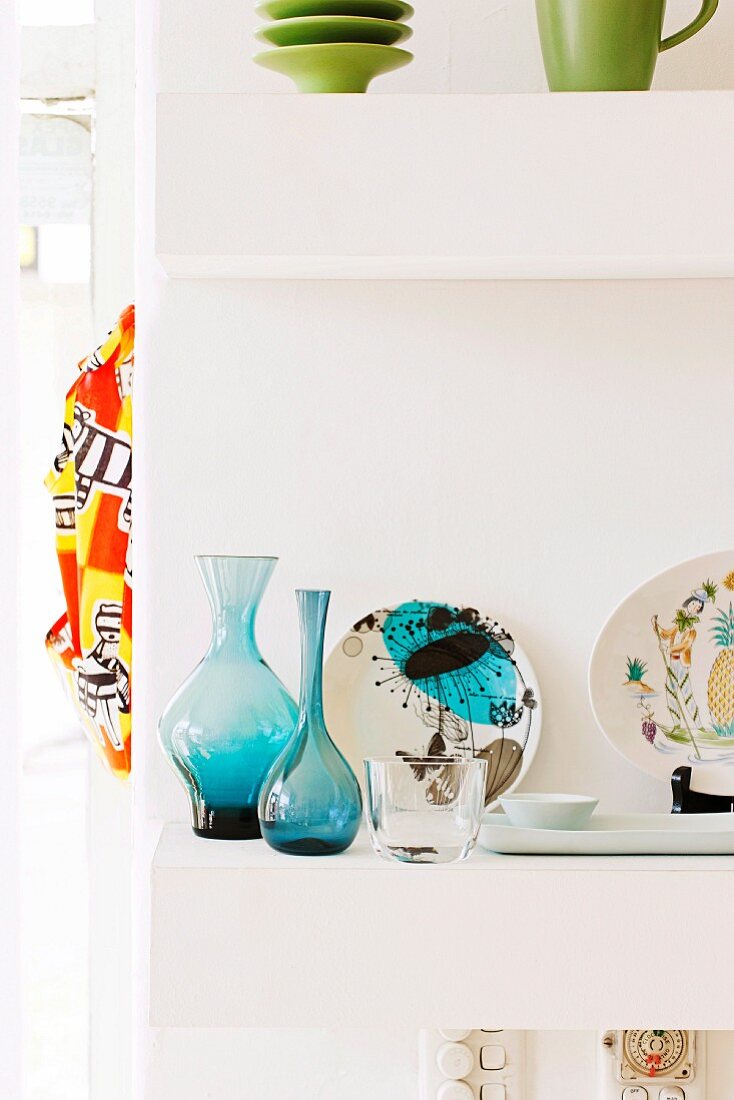 Blue glass vases and painted china plates on white shelves