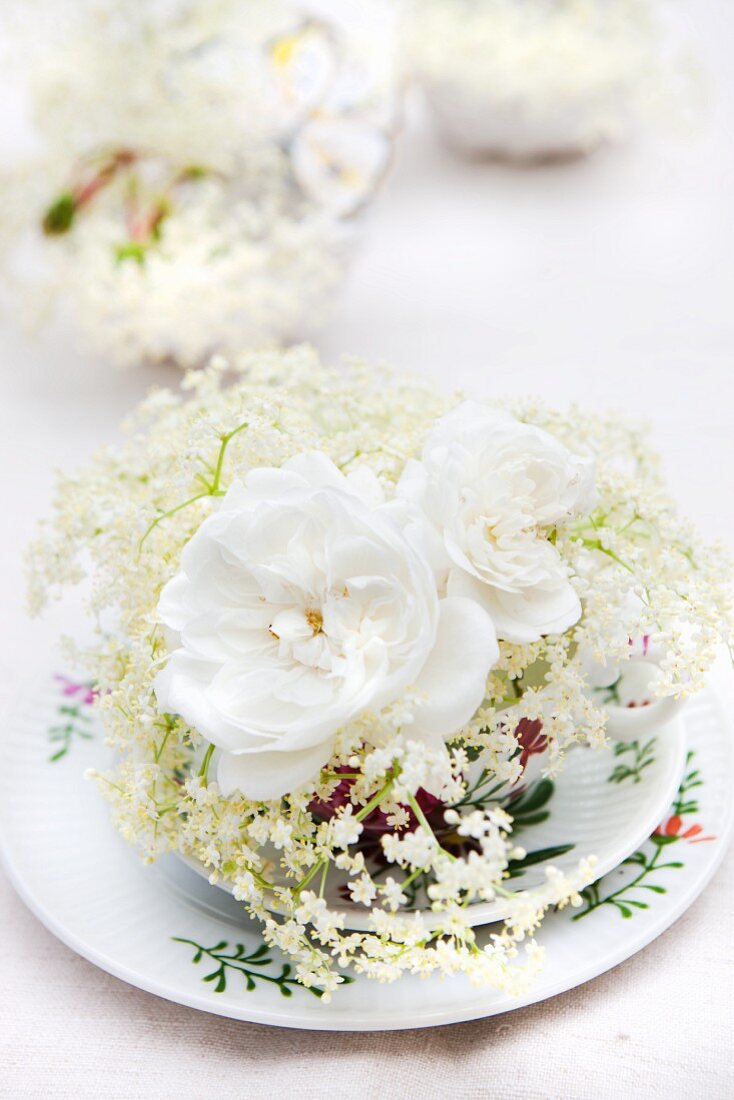 White roses and elder flowers on a place setting with a cup