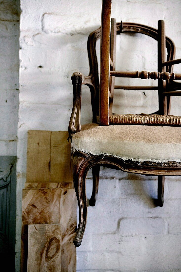 Antike, renovierungsbedürftige Stühle an weiss getünchter Ziegelwand hängend