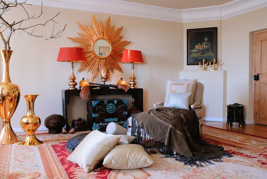 Gemütlicher Sitzplatz mit Kissen und Messing Bodenvasen vor Wandtisch und Spiegel mit strahlenförmigem Goldrahmen in traditionellem Ambiente