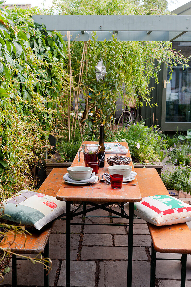 Holzbänke und Tisch auf gepflasterten Terrasse unter Pergola