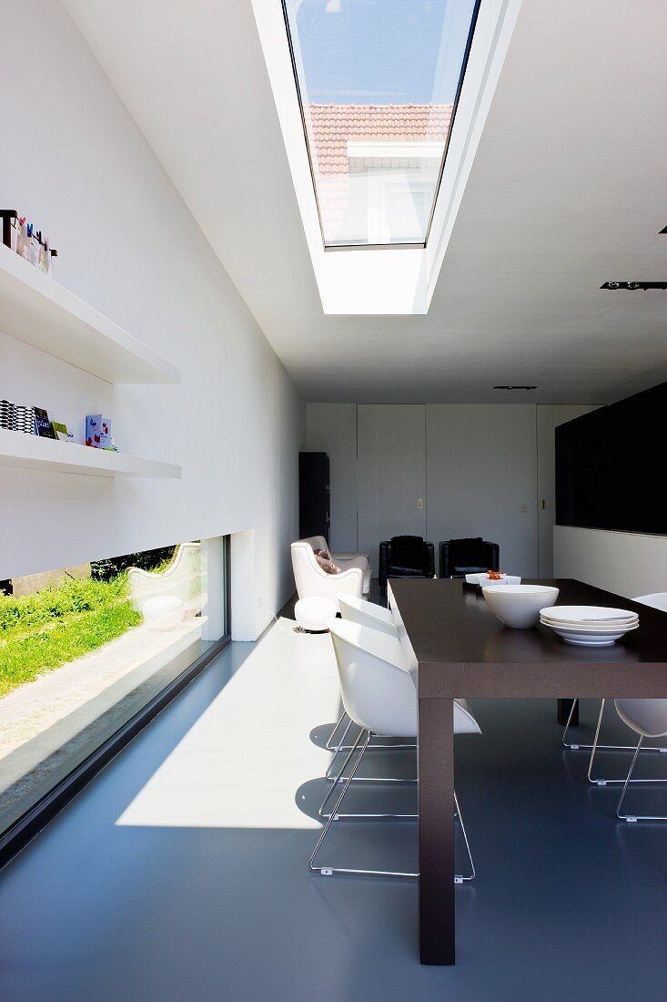 Elegant dining area with overhead skylight and long, large narrow window at the base of the wall