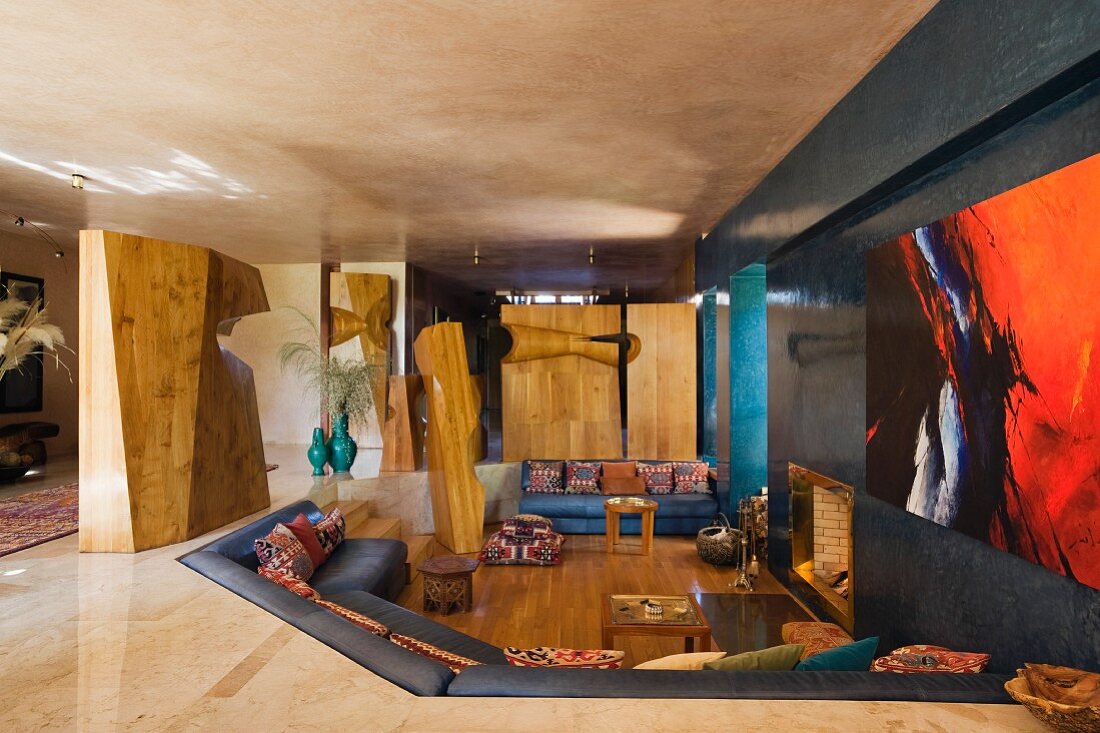 Modernes Wohnzimmer mit Holzskulpturen um tiefergelegten Loungebereich und dunkle Wand mit Kamineinbau