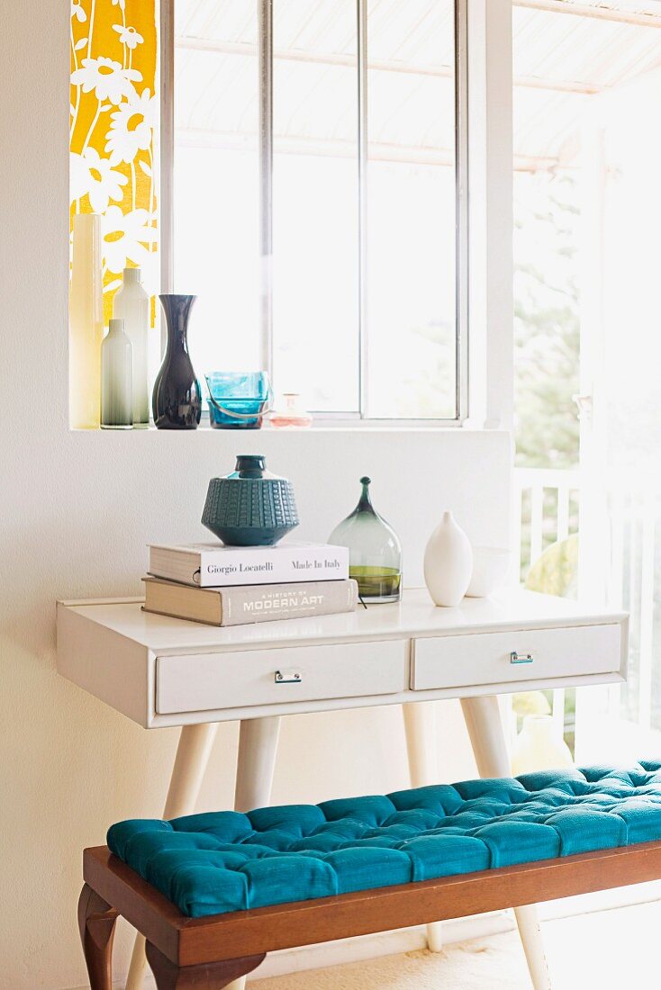 White-painted console table with drawers and bench with blue cushion below window