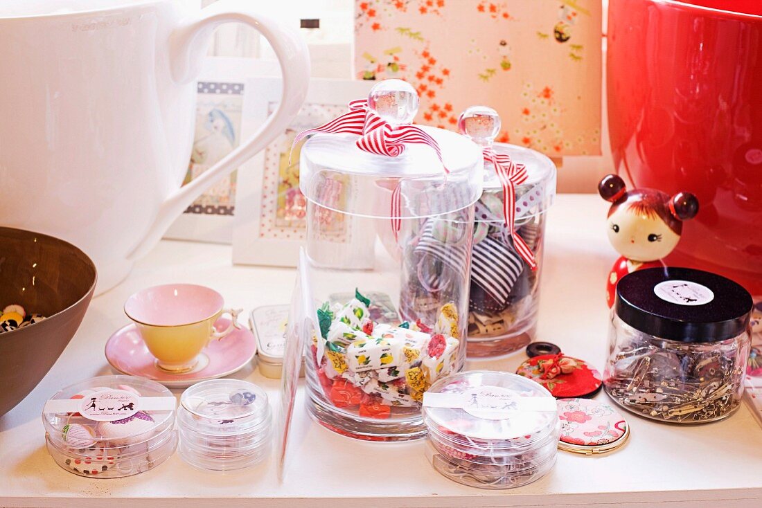 Bonbons, Nähutensilien in Aufbewahrungsgläsern, japanische Puppe, Tasse und Bilderrahmen auf eine Ablage