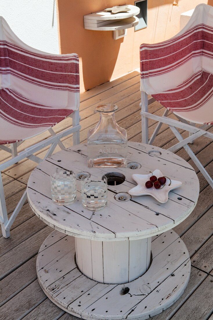 Upcycled table made from old cable reel on wooden terrace between two striped director's chairs