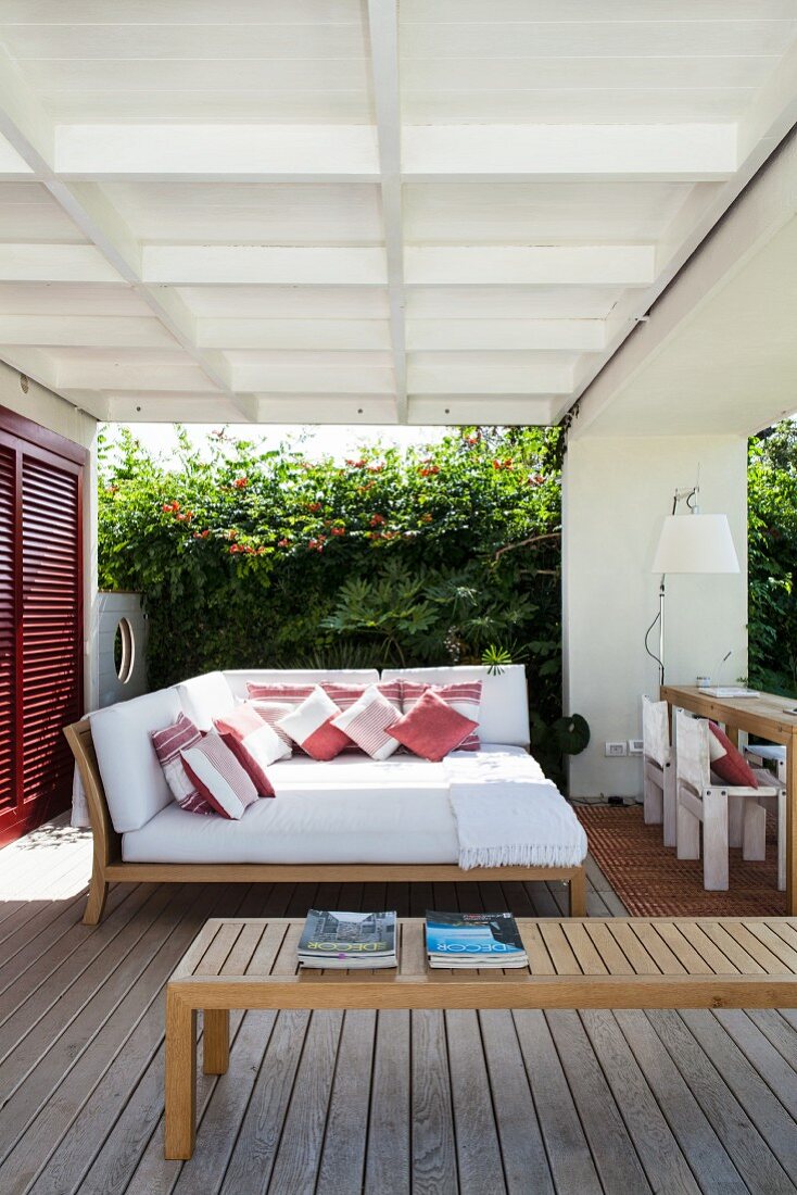 Veranda mit bequemer Liegeinsel vor üppig bewachsener Gartenmauer