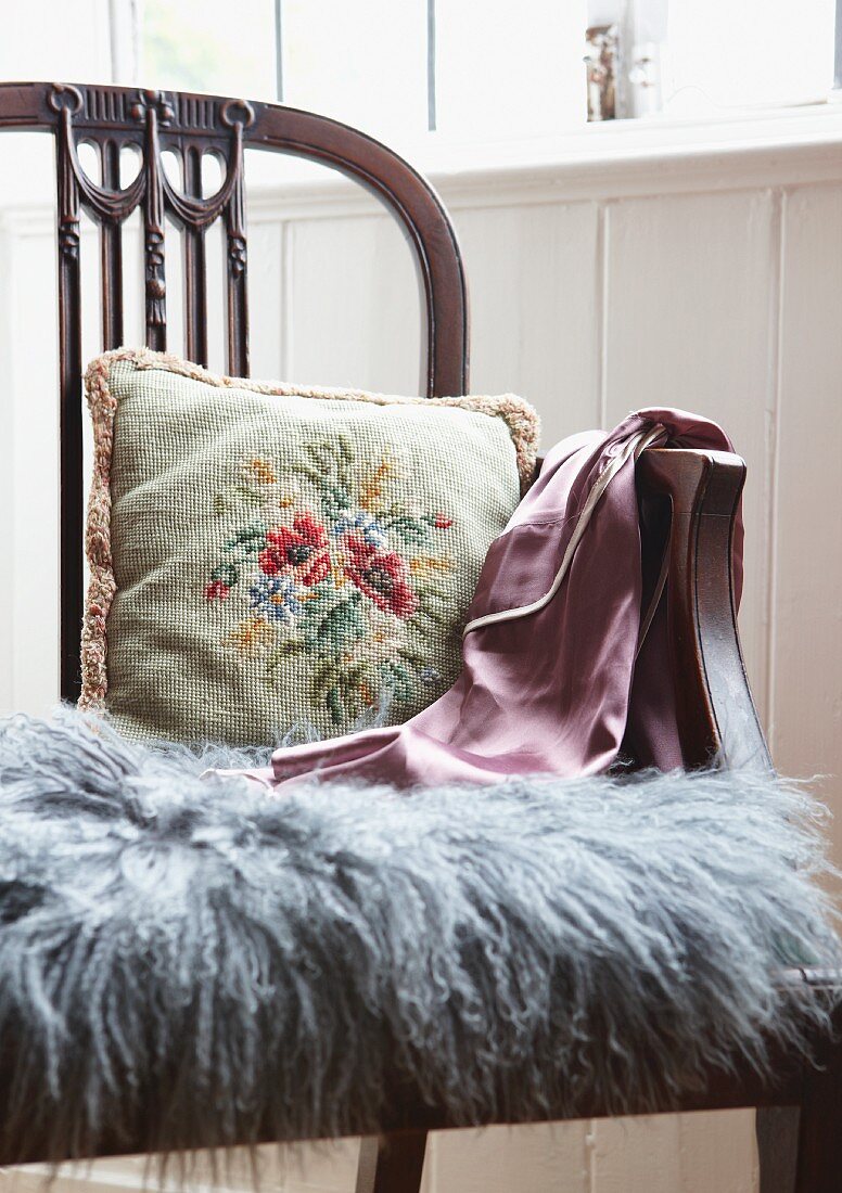Floral besticktes Kissen und grauer Fellstreifen auf antikem Holzstuhl im englischen Stil