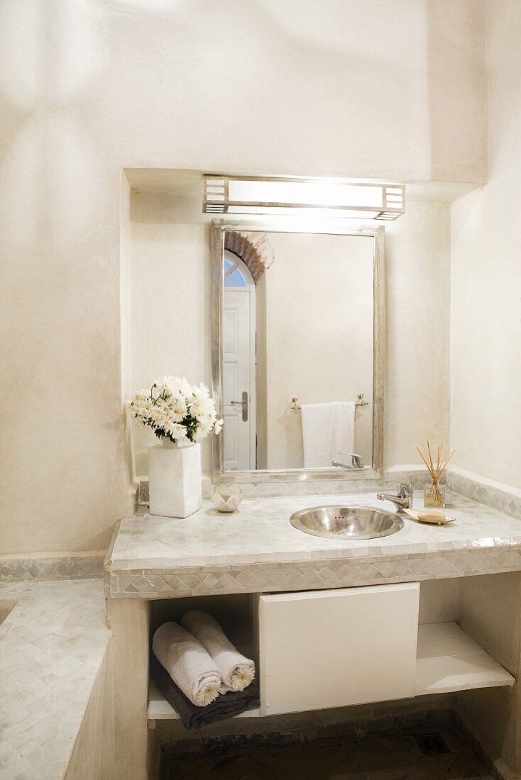 Schlichter Waschtisch aus heller Steinplatte mit eingelassenem Edelstahlbecken und beleuchtetem Spiegel in Wandnische eines orientalischen Bades