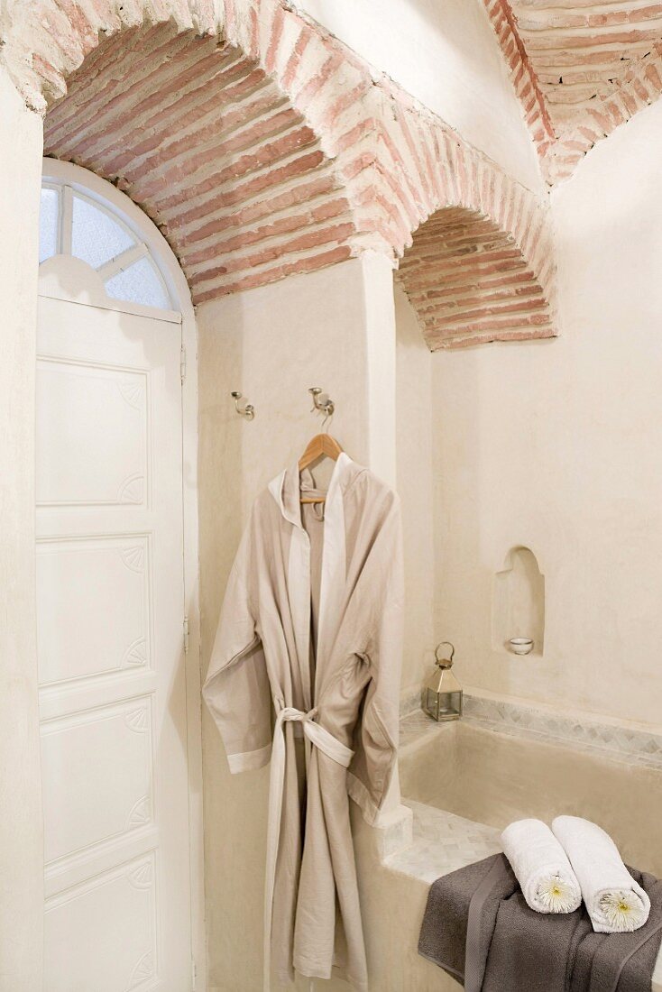 Dressing gown and towels in Oriental bathroom with vaulted brick ceiling and white, panelled arched door with fanlight