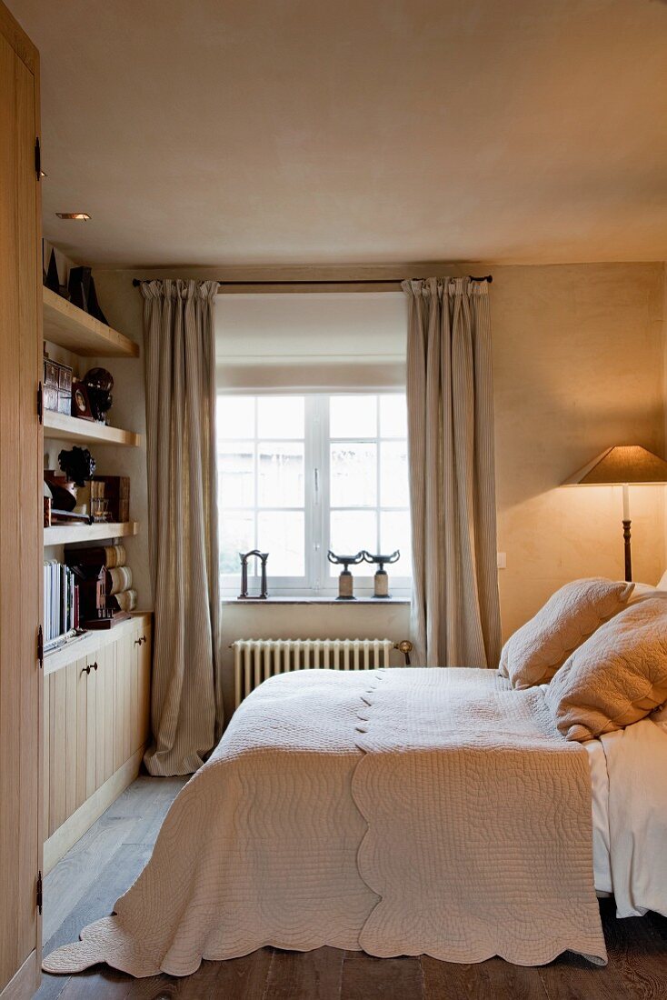 Doppelbett mit dekorativer Steppdecke und passenden Kissen gegenüber einer Regalwand in einem gemütlichen Schlafzimmer
