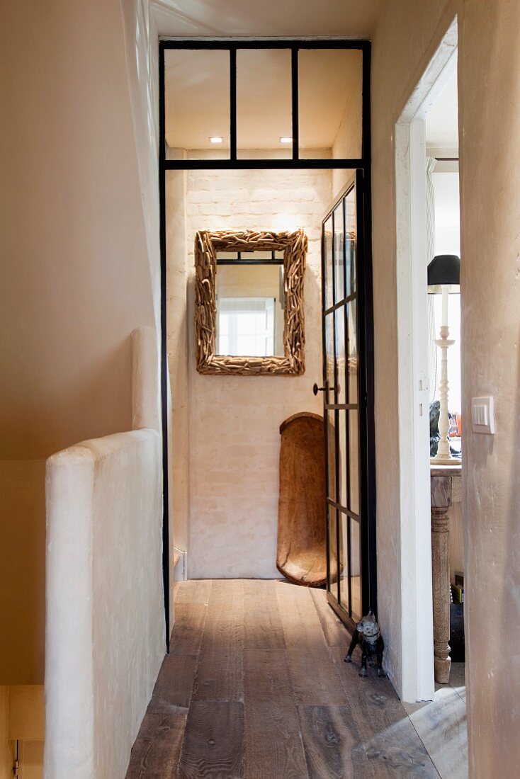 View through a hallway of an old country home with wooden flooring and limestone walls of an open glass door and a wall mirror