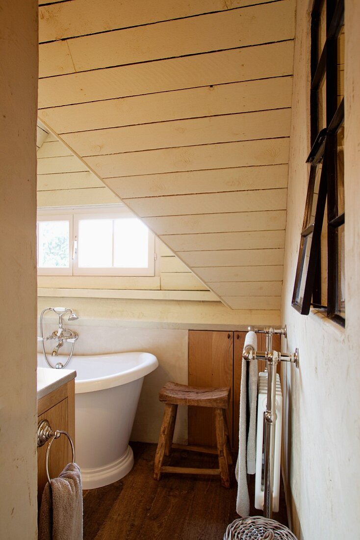 Blick in das elegante Badezimmer eines urigen Landhauses mit holzvertäfelter Dachschräge und dunklem Dielenboden