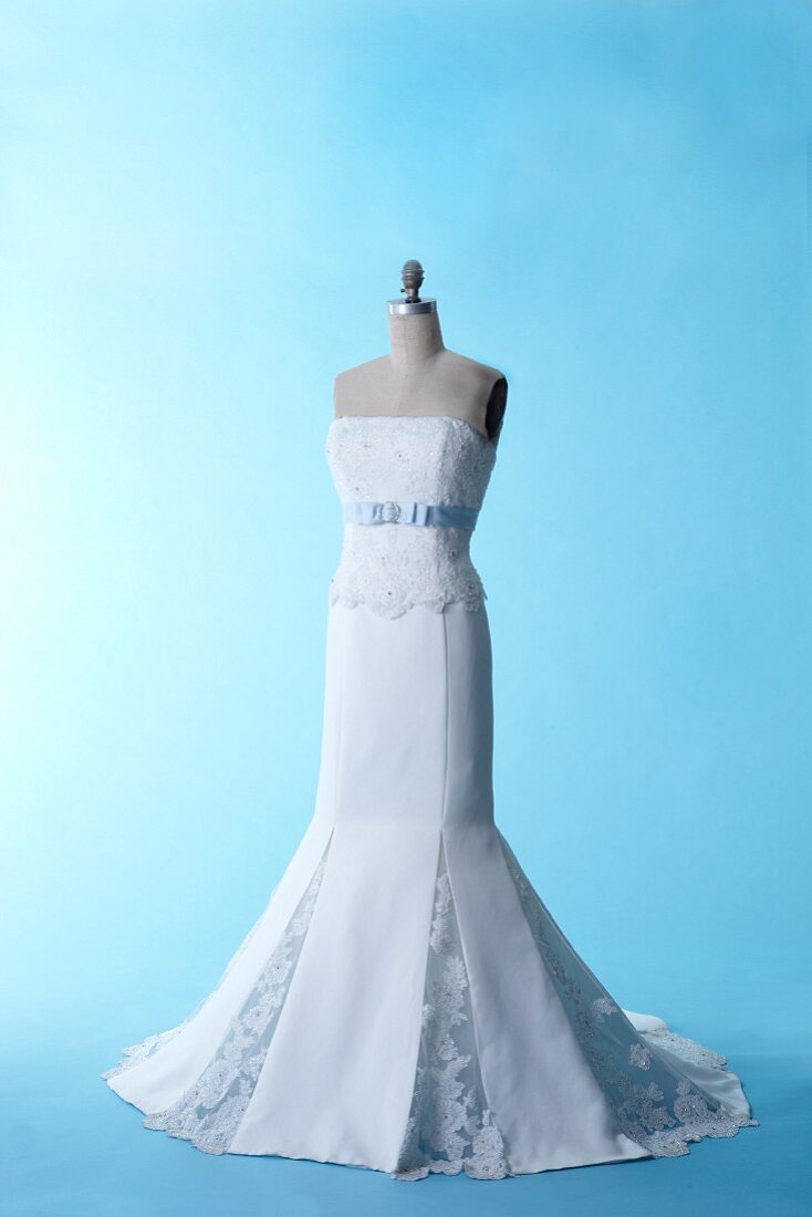 Schneiderpuppe mit ausgestelltem Brautkleid aus Seide und Spitze vor blauem Studiohintergrund