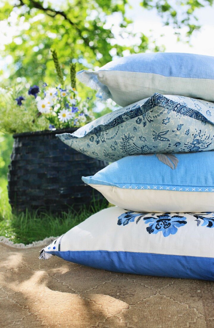 Stapel gemusterter Kissen in Blau-Weiß auf Terrassenplatten in Sommergarten