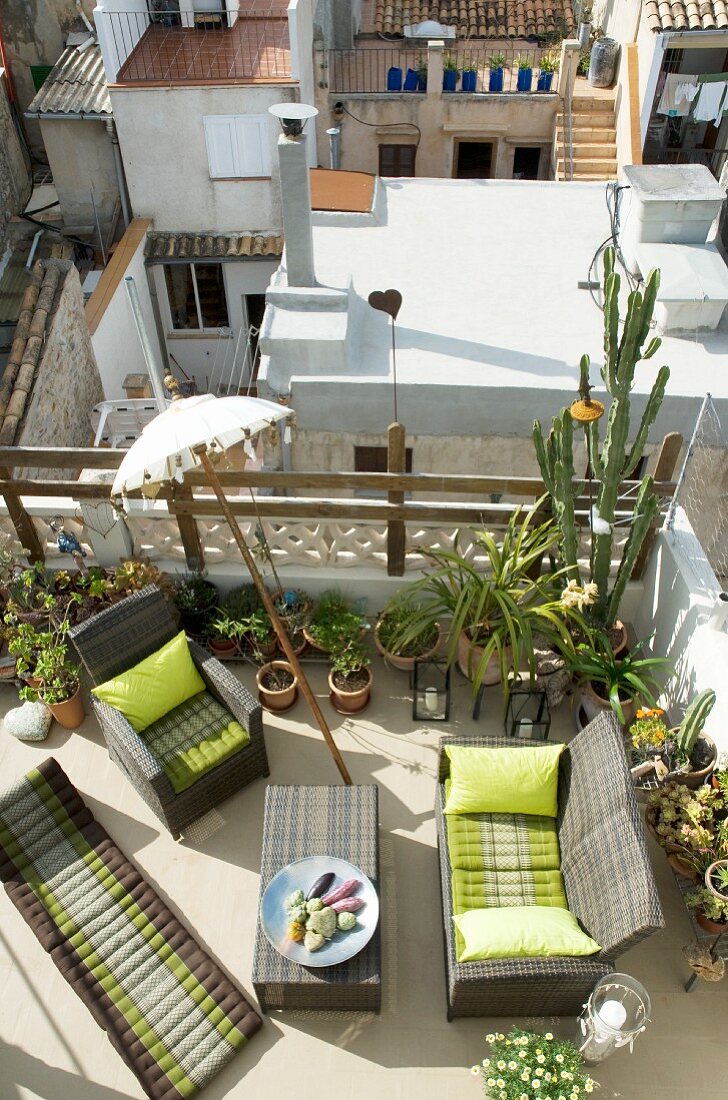 Luftige Dachterrasse mit bequemen Korbmöbeln, vielen Topfpflanzen, indischem Sonnenschirm und mit Blick auf die Nachbarterrassen