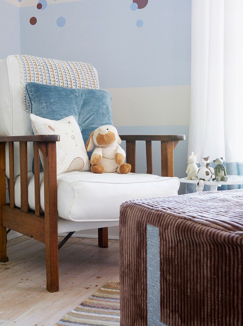 Kinderzimmerecke mit Polsterlehnstuhl vor hellblau-weiß gestrichener Wand und einem großen Sitzwürfel mit braunem Cordbezug; verschiedene Plüschtiere zieren das gemütliche Ambiente