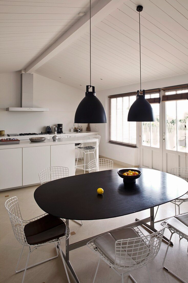 Retro hanging lamps above a dining table with a black top and chairs with white metal frames in a functional kitchen