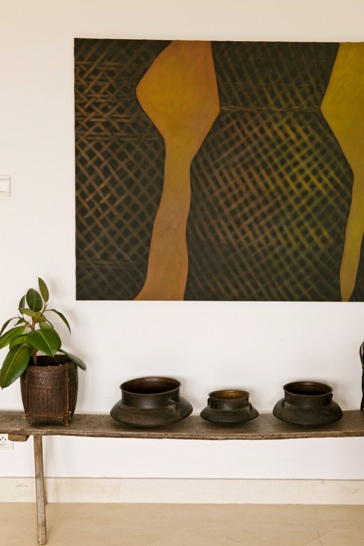 Dark containers on a rustic bench under a modern painting with a gold colored wall