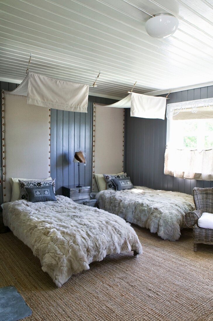 Doppelzimmer mit gemütlichen Felldecken und Kissen auf den Betten, darüber abgehängte weiße Stoffbahnen als Baldachine, Rückenlehne an der Wand gepolstert