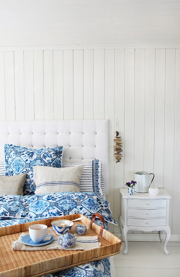 Weisses Bett mit blau-weisser Bettwäsche und Leinenkissen; auf dem Bett ein Frühstückstablett