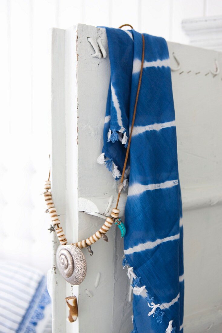 Blue and white batik cloth and necklace with shell pendant hanging over door of vintage cupboard