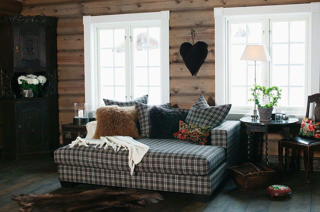 Tagesbett mit kariertem Bezug und passenden Kissen vor Sprossenfenster mit weisser Zarge in Holzhaus