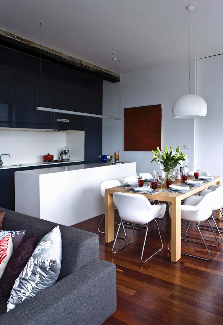 Offener Wohnraum mit gedecktem Esstisch vor schwarzweisser Einbauküche; Ecke eines grauen Sofas im Vordergrund