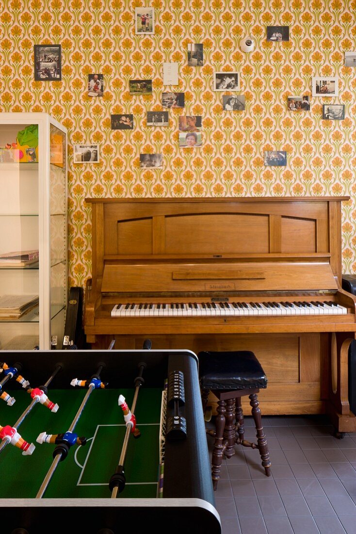 Foosball across from a piano along a wall with patterned wallpaper