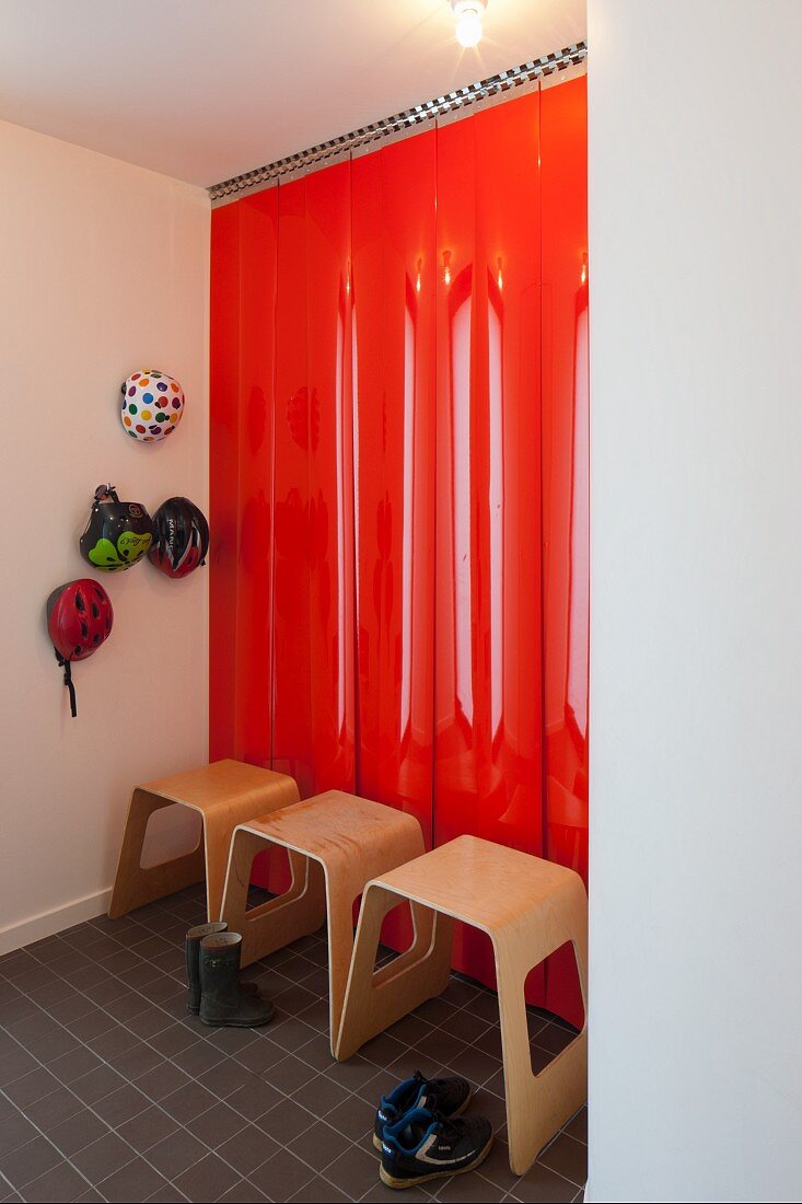 Moderne Holzhocker vor rot lackierten Paneelen an Wand und aufgehängte Fahrradhelme