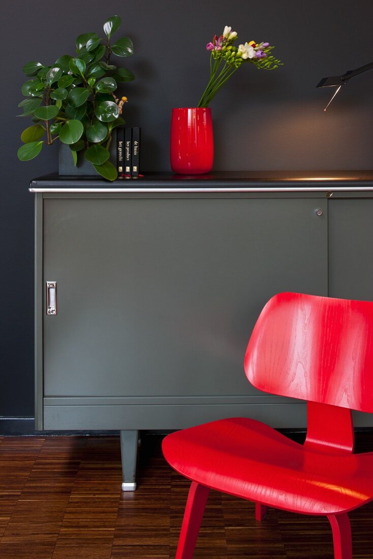 Roter Klassiker Stuhl vor grauem Designer Sideboard an schwarzer Wand
