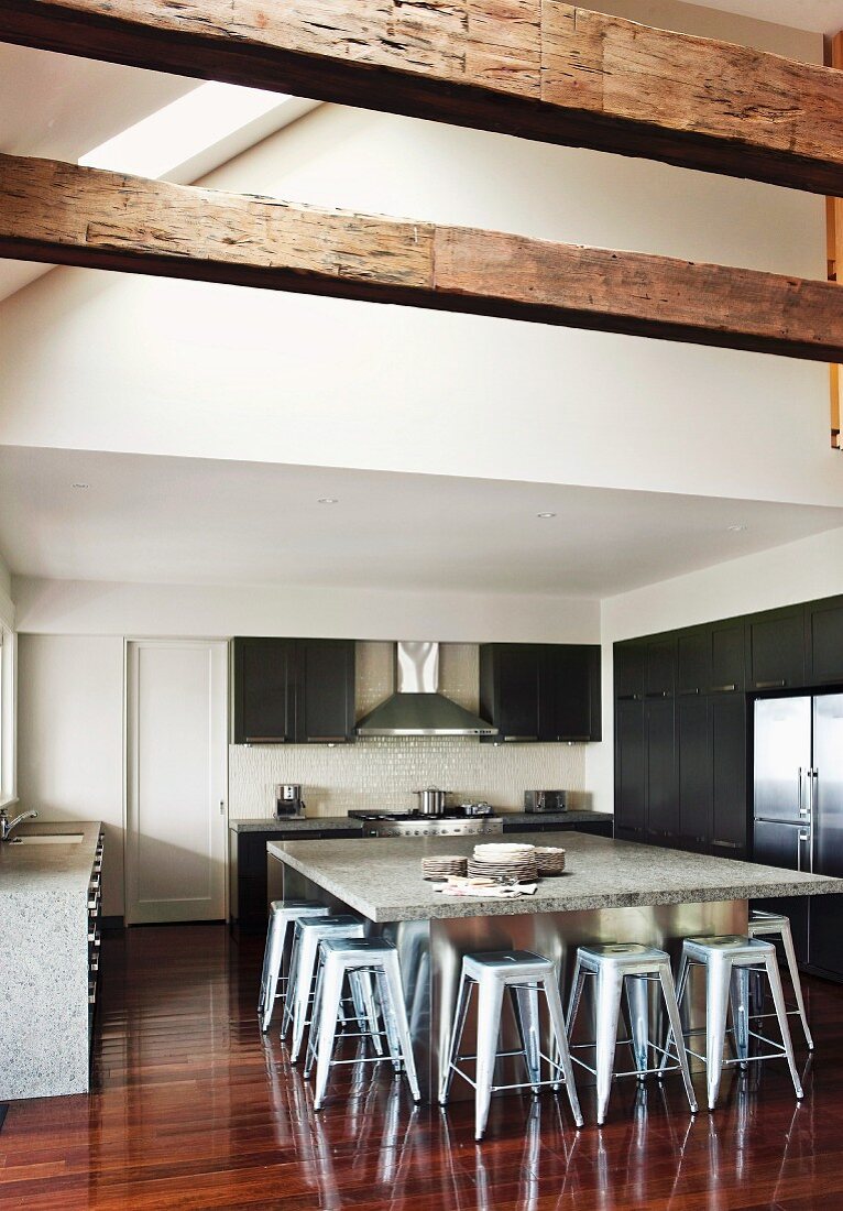 Offene Küche in großzügigem Dachraum mit Metallhockern an ausladendem Tischblock mit Steinplatte