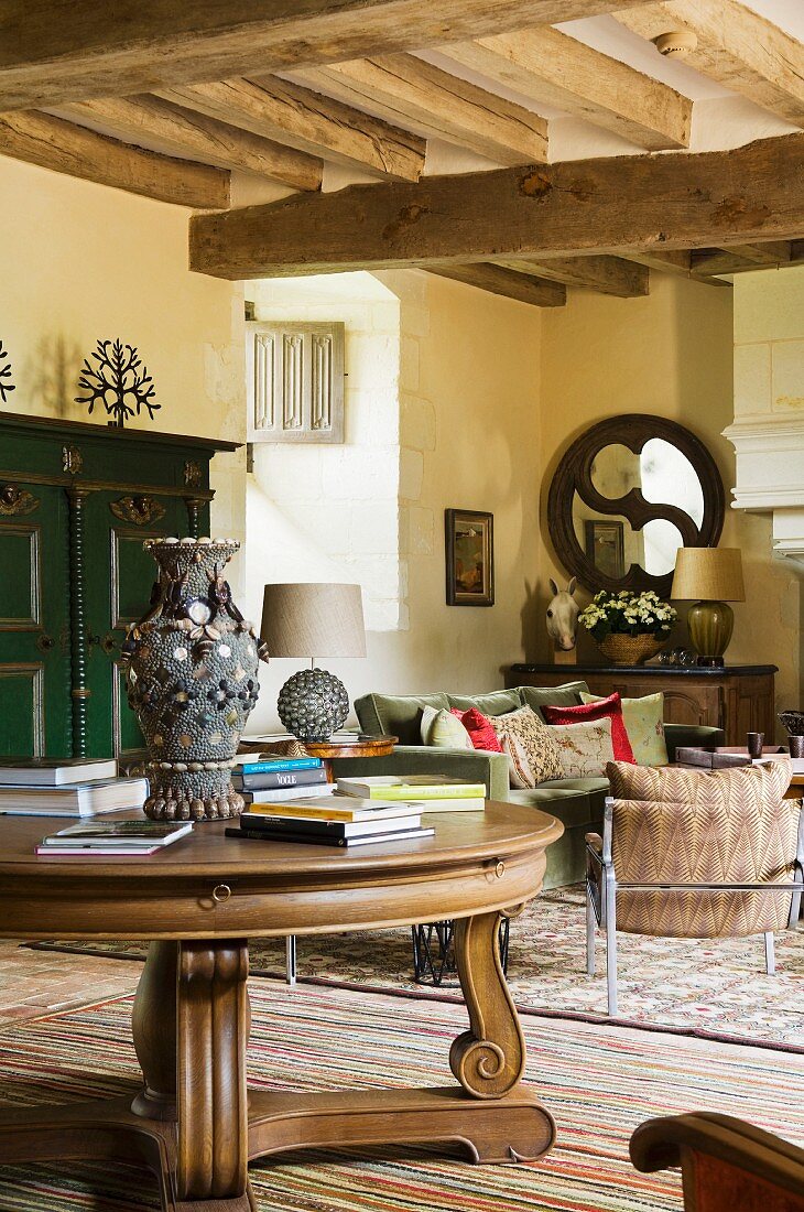 Antique, round wooden table in front of lounge area in Mediterranean country house with wood-beamed ceiling