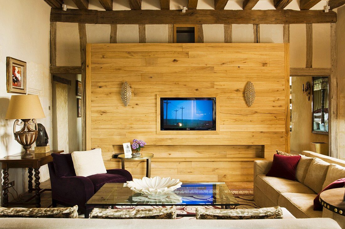 Schlichtes Sofa und Sessel am Couchtisch mit Glasplatte vor Holz Raumteiler mit integriertem Fernseher