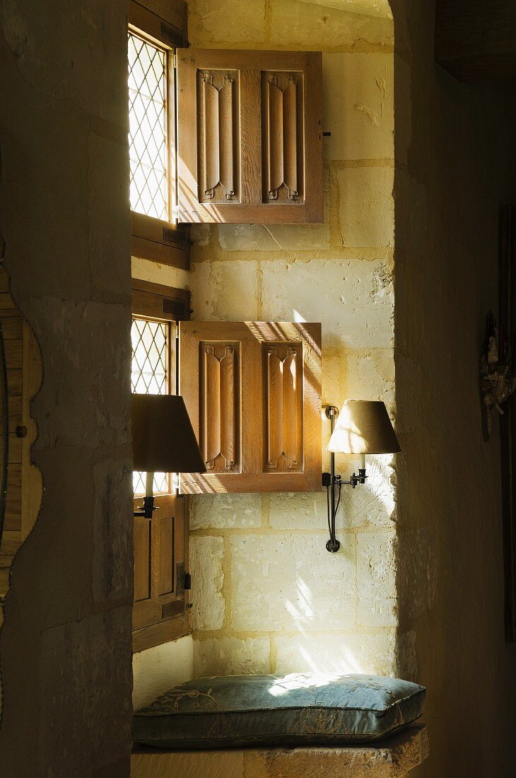 Geteilte Fensterinnenläden am Fenster und Wandleuchten an Natursteinwand