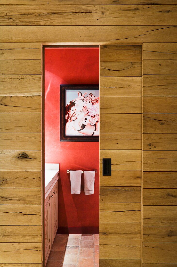 Simple wooden wall with open sliding door and view of picture on red wall in bathroom