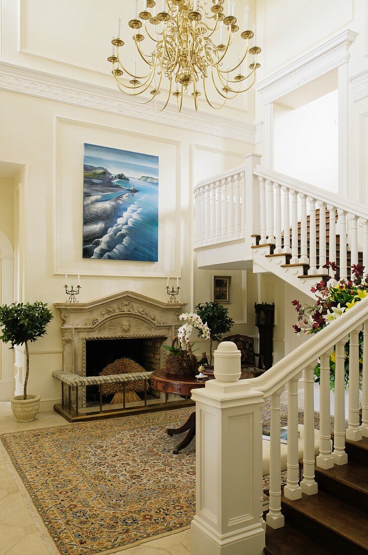 Grand foyer with staircase and modern artwork on white, wood-panelled wall above open fireplace