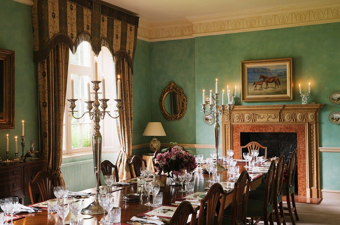 Lange Tafel mit Gedecken und silbernen Kerzenständern in herrschaftlichem Esszimmer mit blau-grün getönten Wänden