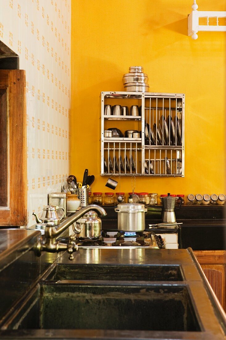 Kitchen counter with vintage tap fittings over sink and crockery in drying rack hung on yellow wall