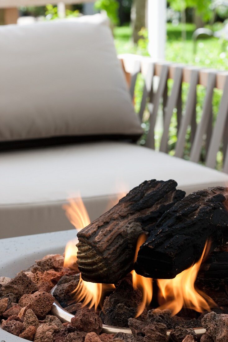 Modern outdoor fire pit with burning logs in front of an upholstered chair