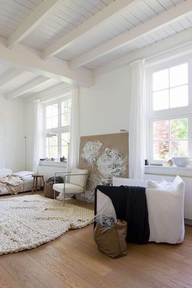 Tasche auf Boden neben weißem Polstersessel in schlichtem Wohnzimmer mit weisser Holzdecke