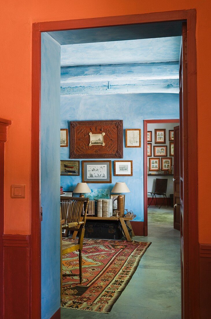 Blick durch roten Türrahmen in pastellblaues Arbeitszimmer mit pastellblau übertünchten Holzbalken und orientalischem Teppich