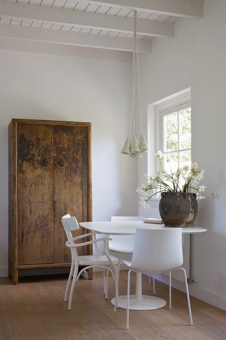 Simple chair and modern shell chairs at a white table in front of a rustic farmhouse cupboard