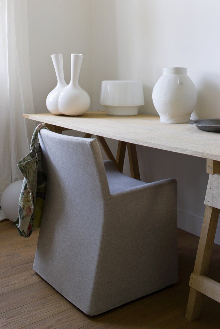 Stuhl mit grauer Husse am schlichten Arbeitstisch und weiße Vasen in verschiedenen Stilen