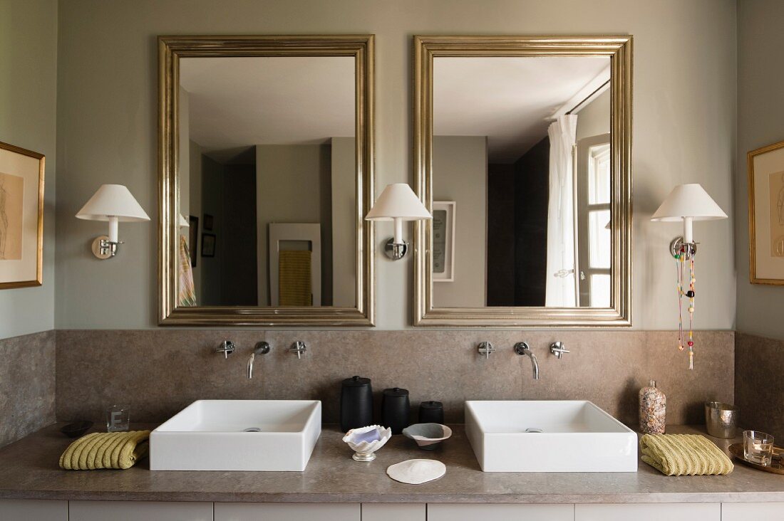 Wandlämpchen zwischen gerahmten Spiegeln und Natursteinverkleidung mit modernen Waschbecken
