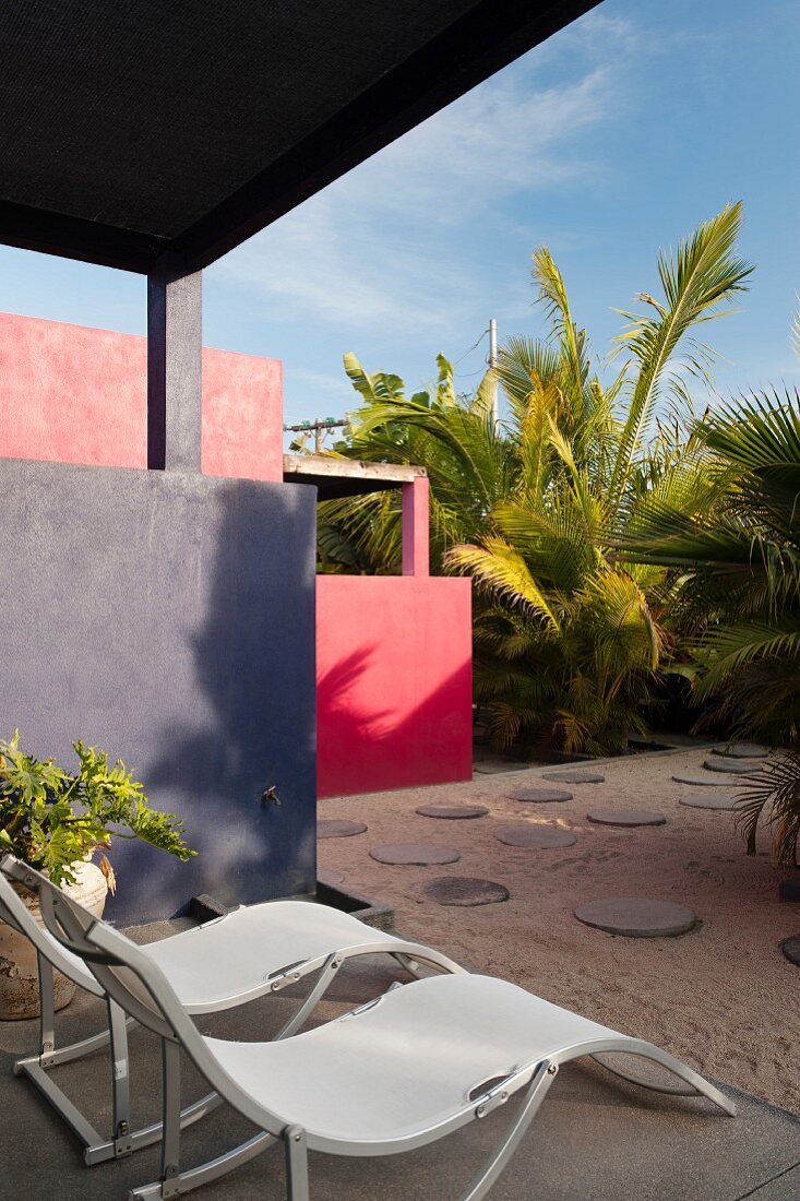 Moderne Liegestühle auf der Terrasse mit Blick auf den Innenhof mit runden Pflastersteinen und Palmen