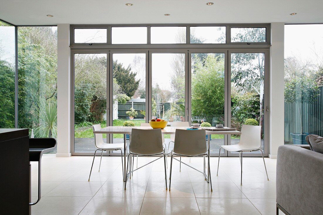 Modern dining table with chairs in front of a bank of windows and view into the garden